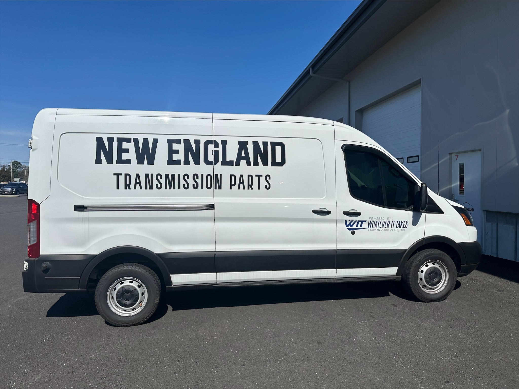 New England Transmission Parts delivery van with the WIT partner logo, parked outside an industrial building